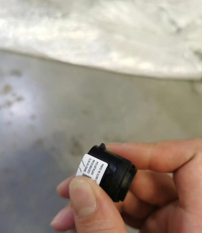 Hand holding a Zeekr EV radar sensor with label, in a workshop environment